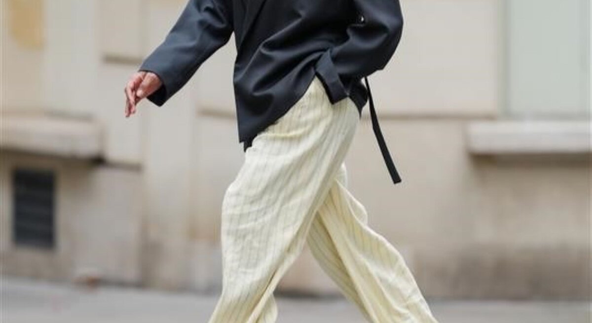 Zu sehen ist eine Frau, die eine Hose in Buttergelb und ein graues Oberteil trägt