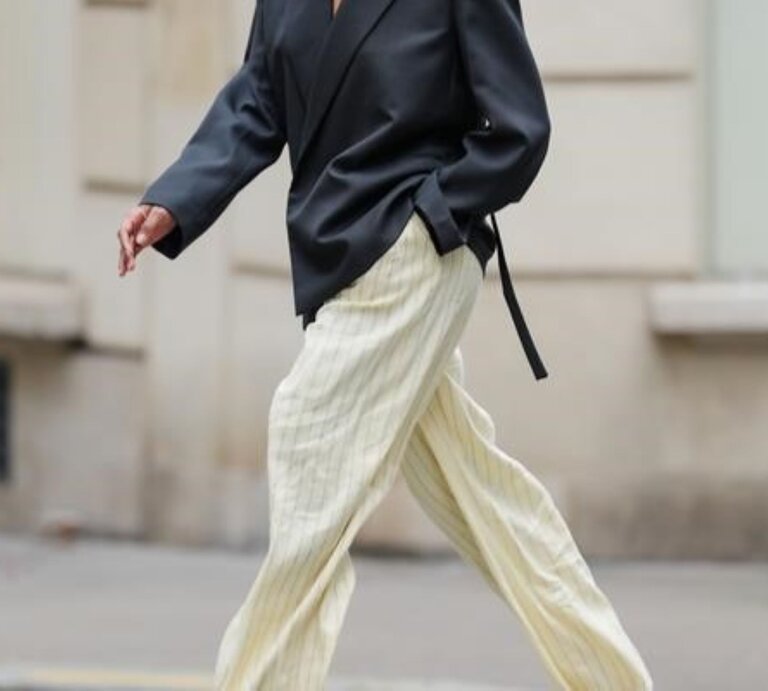 Zu sehen ist eine Frau, die eine Hose in Buttergelb und ein graues Oberteil trägt | © GettyImages/Edward Berthelot 