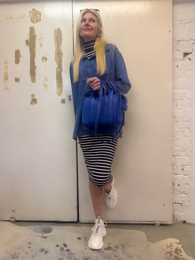Stylishe Frau mit langen blonden Haaren trägt schwarz-weiß gestreiftes Kleid, Jeanstunika und Marc-Jacobs-Tasche. | © Renate Zott