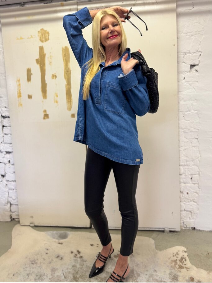 Blondhaarige Frau mit Jeanstunika, schwarzer Lederleggings und spitzen Pumps lächelt und hält Sonnenbrille hoch. | © Renate Zott