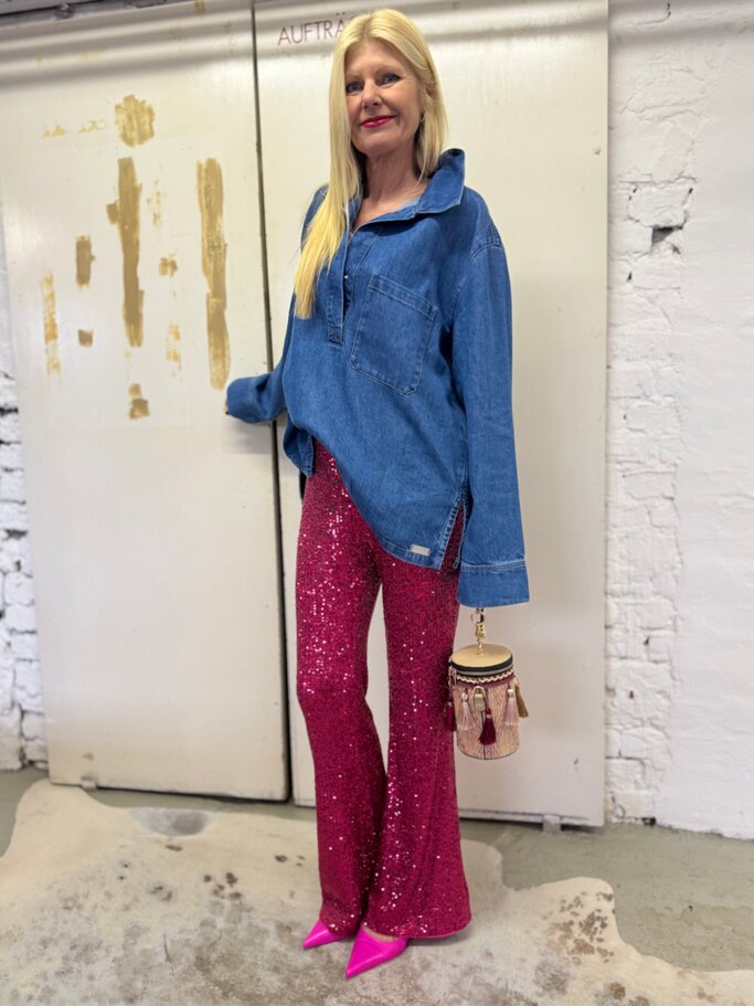 Stylishe Frau mit langen blonden Haaren kombiniert oversized Jeanstunika mit Paillettenhose und knallpinken Schuhen. | © Renate Zott