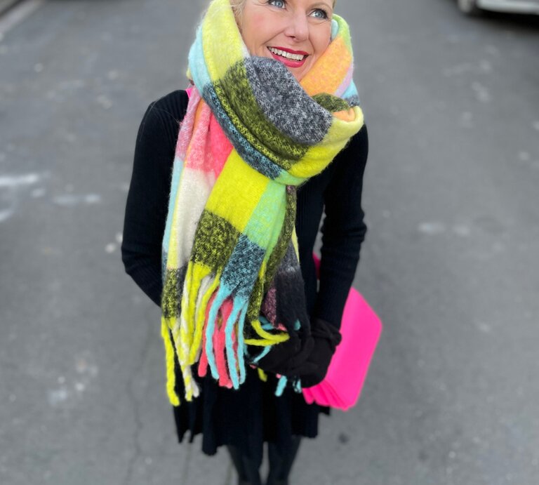 Renate Zott mit hochgestecktem Haar, buntem XXL-Schal und schwarzem Outfit steht auf einer Stadtstraße mit geparkten Autos. | © Renate Zott