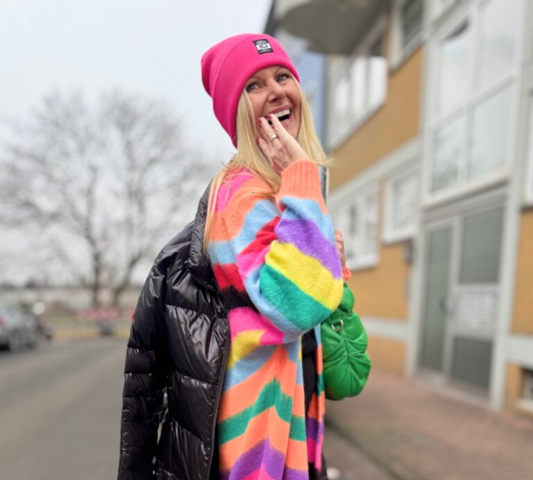 Renate Zott mit farbenfrohem Outfit, grüner Handtasche und schwarzen Plateau-Boots blickt strahlend über die Schulter. | © Renate Zott
