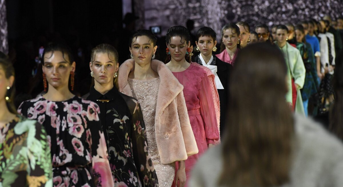 Eine Reihe von Models in eleganter Designermode mit floralen Mustern, Pastelltönen und luxuriösen Stoffen läuft über den Laufsteg.