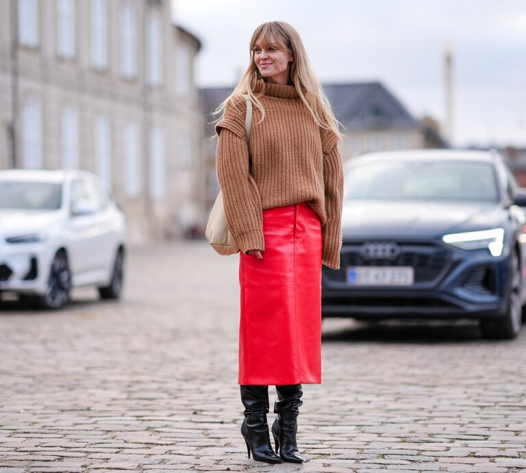 Streetstylefoto von Frau in rotem Lederrock. Zusätzlich trägt sie einen hellen Strickpullover mit Rollkragen | © Edward Berthelot/Getty Images