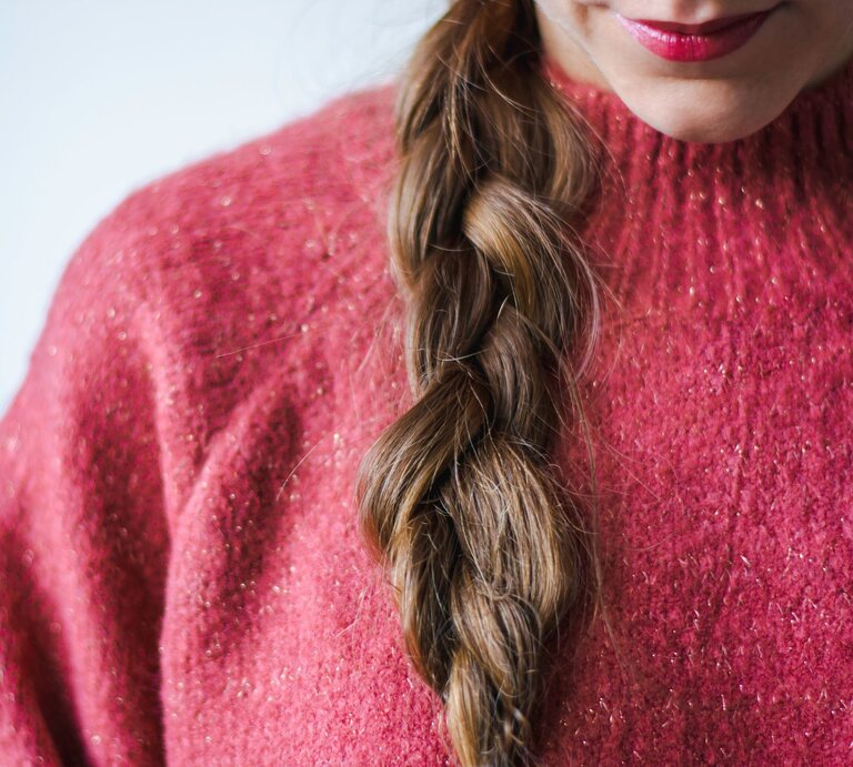 Eine Frau mit geflochtenem braunem Haar trägt einen rosafarbenen Glitzerpullover und dezenten Lippenstift. | © Adobe Stock/ Evelien