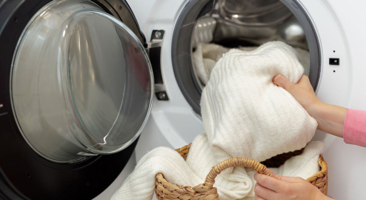 Zu sehen ist eine Waschmaschiene mit einem Wollpullover und Frauenhände