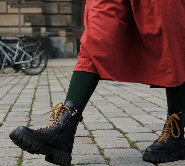 Schwarze klobige Dr Martens Stiefel mit senffarbenen Schnürsenkeln, getragen zu grün-schwarzen Strumpfhosen und einem roten Rock auf Kopfsteinpflaster. | © Getty Images/ Zheka-Boss