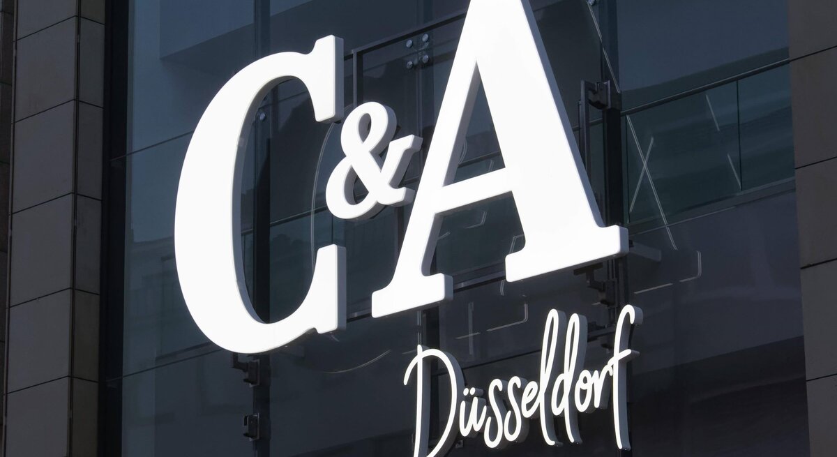 Leuchtendes C&A-Logo mit Schriftzug "Düsseldorf" an einer Glasfassade mit Spiegeleffekt.