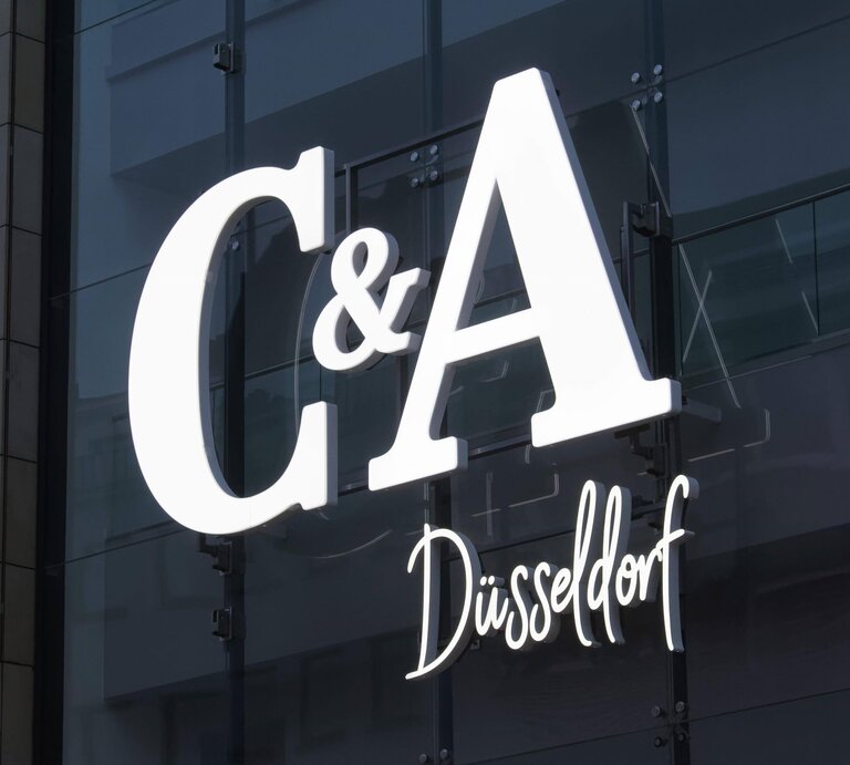Leuchtendes C&A-Logo mit Schriftzug "Düsseldorf" an einer Glasfassade mit Spiegeleffekt. | © IMAGO / imagebroker