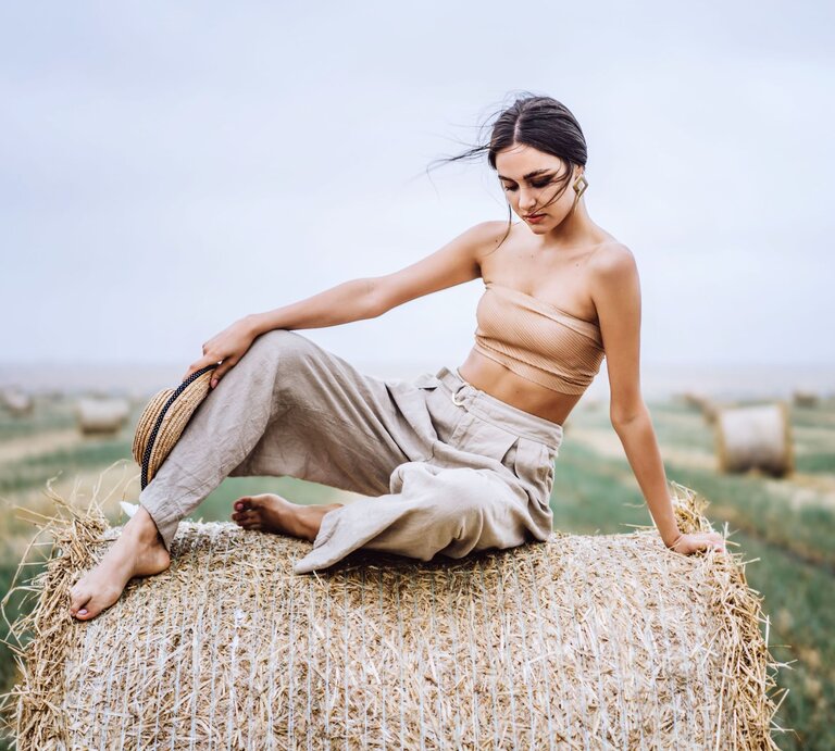 Zu sehen ist die brunette Frau auf einem Heuballen, die eine Leinenhose trägt | © Shutterstock/ bedya