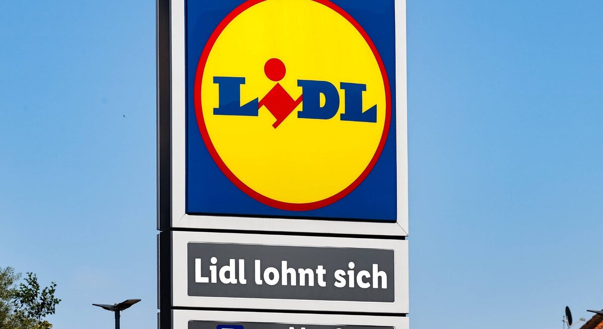 Ein Schild mit dem Lidl-Logo und dem Slogan "Lidl lohnt sich" vor klarem, blauem Himmel und Gebäuden im Hintergrund.