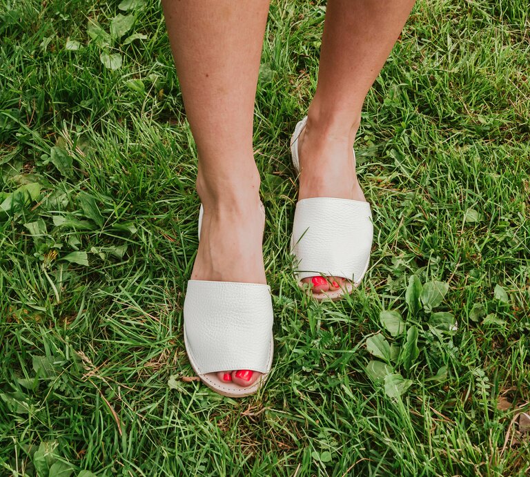 Weibliche Füße mit rotem Nagellack in weißen Espadrilles-Sandalen stehen auf frisch gemähtem, saftig grünem Rasen. | © Adobe Stock/ Ксения Фалёва