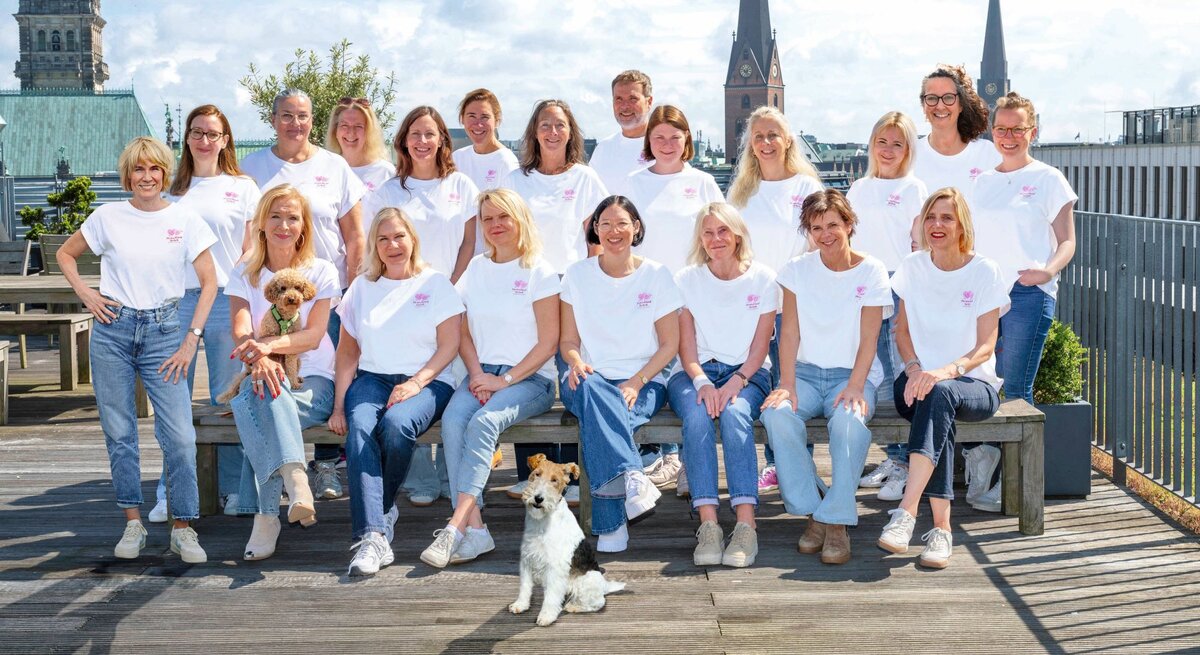 Das BILD der FRAU Team in weißen T-Shirts und Jeans posiert auf einer Dachterrasse vor dem Hamburger Rathaus, zwei Hunde sitzen dabei.