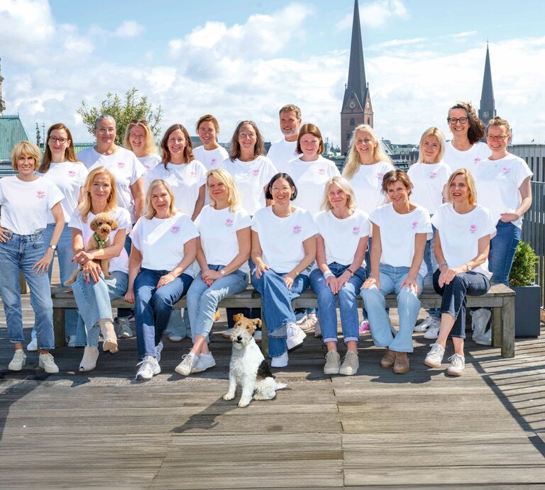 Das BILD der FRAU Team in weißen T-Shirts und Jeans posiert auf einer Dachterrasse vor dem Hamburger Rathaus, zwei Hunde sitzen dabei. | © Bild der Frau/ Ulrike Schacht