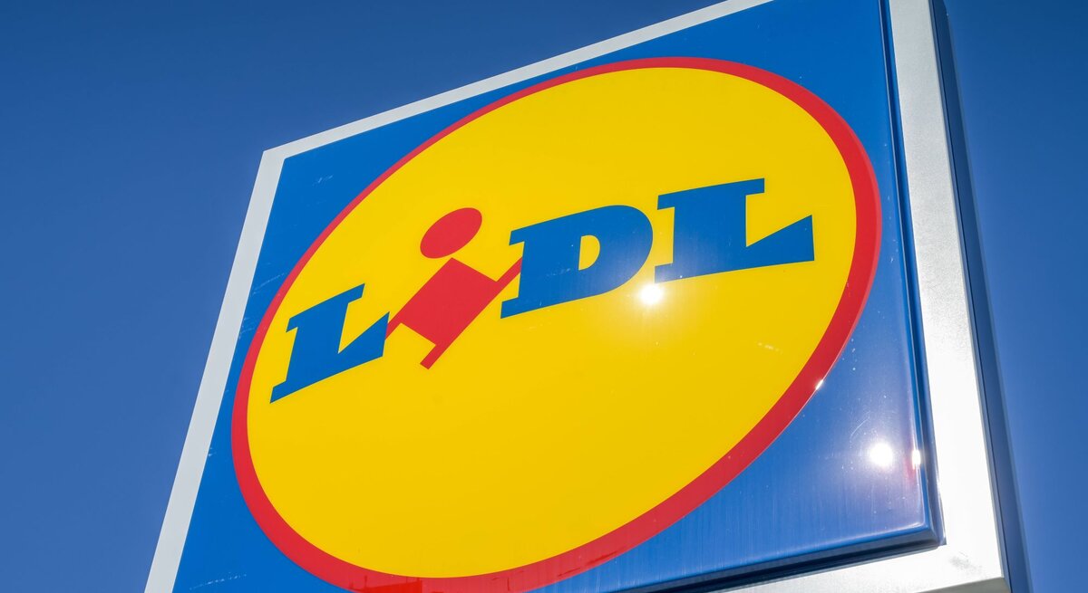 Sonnenstrahlen spiegeln sich auf einem scharf fokussierten Lidl-Logo unter blauem Himmel.