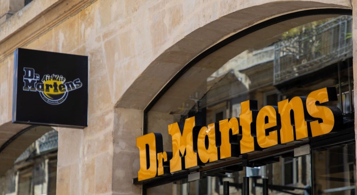 Dr. Martens-Geschäftsschild mit gelbem Schriftzug auf einem modernen Geschäftseingang aus Glas und Stein.