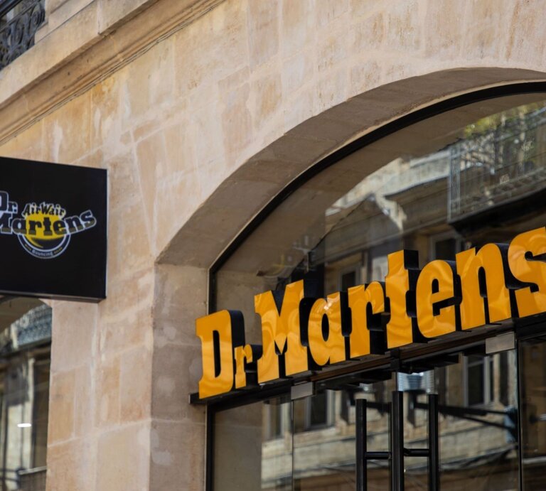 Dr. Martens-Geschäftsschild mit gelbem Schriftzug auf einem modernen Geschäftseingang aus Glas und Stein. | © Adobe Stock/ OceanProd