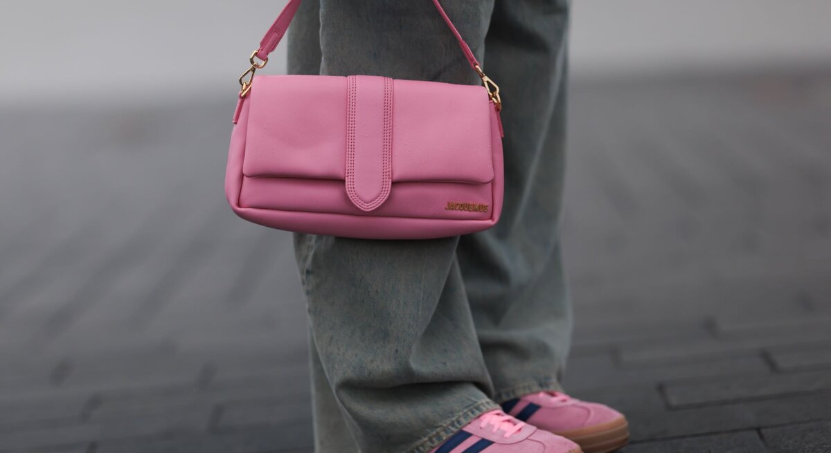 Detailaufnahme einer rosa Handtasche mit goldener Schnalle, getragen zu lässiger Jeans und farblich abgestimmten Sneakers.