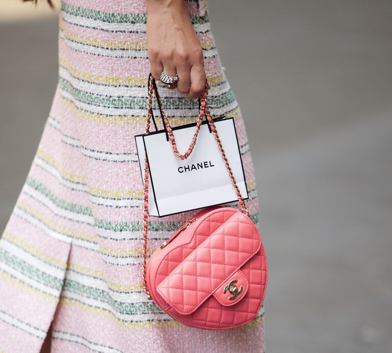 Frau in pastellfarbenem gestreiftem Rock hält eine rosa Chanel-Tasche und eine Chanel-Papiertüte. | © Raimonda Kulikauskiene/Getty Images