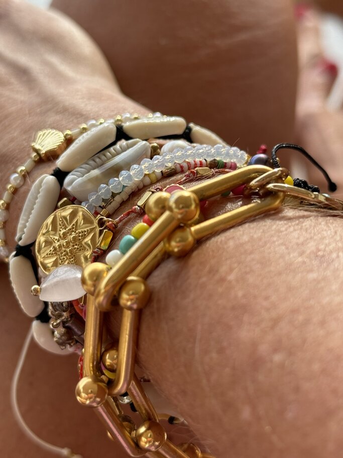 Nahaufnahme von einem Handgelenk, das mit einer Vielzahl von bunten und vielseitigen Armbändern geschmückt ist. Zu sehen sind verschiedene Materialien und Designs, darunter Perlen, Goldglieder, Muschelstücke und Anhänger mit maritimen Motiven.  | © Renate Zott 