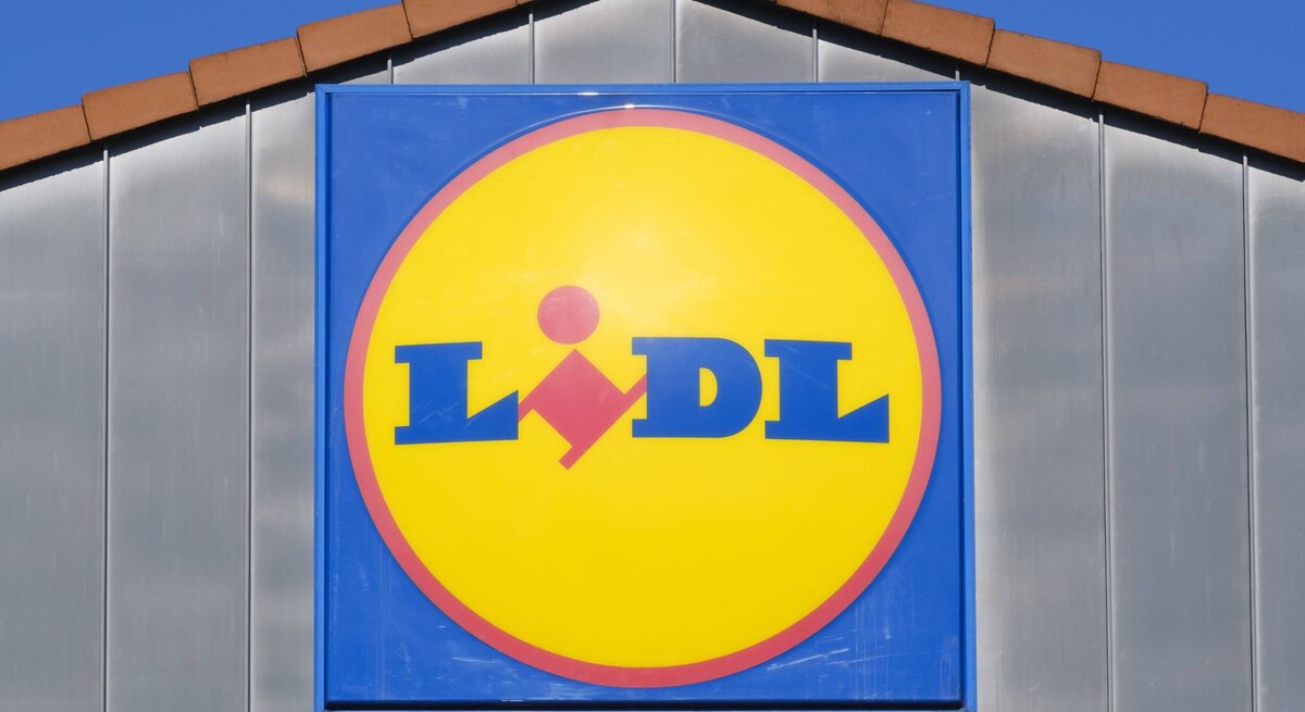 Leuchtendes Lidl-Logo auf blauem Schild, montiert an einer Fassade unter blauem Himmel.