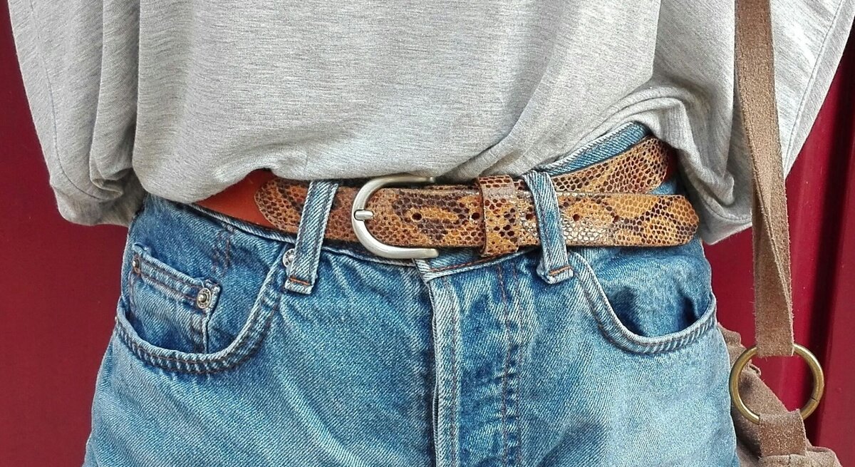 Frau in Jeans: Von ihr sind nur die vorderen Taschen der Hose, der Gürtel und ein Stück vom Oberteil zu sehen, das in die Jeans gestopft ist.