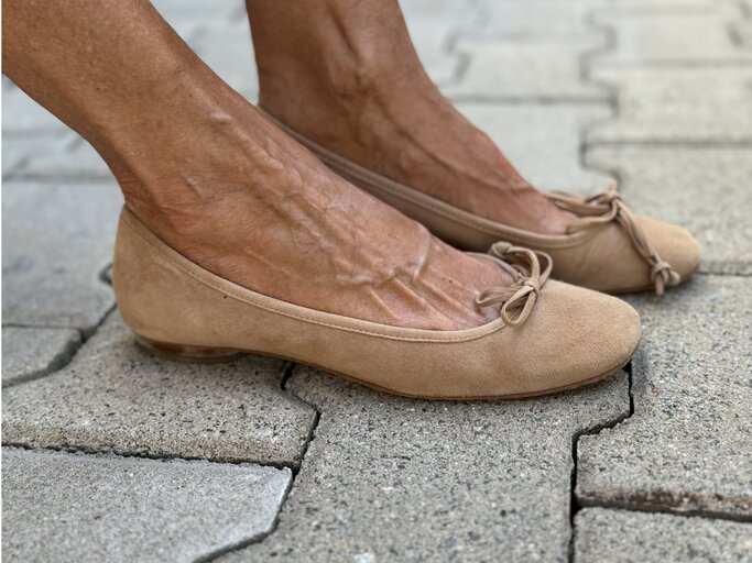 Beine, die in beige Ballerinas stecken. Die Schuhe haben kleine Schleifen an der Vorderseite und bestehen aus Wildleder oder einem ähnlichen Material.  | © Renate Zott