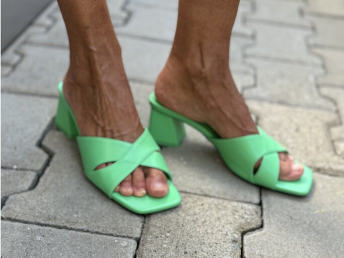 Beine, die in grünen Mules stecken. Diese Schuhe haben einen niedrigen Blockabsatz und breite, sich kreuzende Riemen über den Zehen.  | © Renate Zott