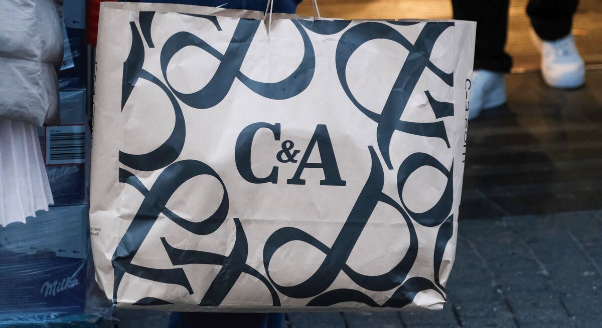 Detailaufnahme einer Einkaufstasche mit C&A-Schriftzug, im Hintergrund unscharfe Passanten.