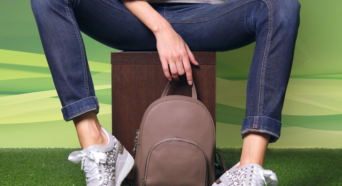 True blue Jeans an den Beinen, sitzend auf einem Hocker. Weiße Sneaker an den Füßen, verschränkte Arme.