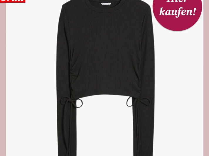  Auf dem Bild ist ein schwarzes Langarmshirt mit Raffungen und Bindebändern an den Ärmelenden dargestellt. Das Shirt ist vor einem weißen Hintergrund mit rosa Umrandung zu sehen, was einen sanften Kontrast zum dunklen Stoff bildet. In der oberen linken Ecke ist das Logo "Bild der Frau" platziert, und in der oberen rechten Ecke befindet sich ein kreisförmiger, magentafarbener Button mit der Aufschrift "Hier kaufen!". Das Oberteil erscheint einfach und stilvoll, vielseitig für verschiedene Anlässe kombinierbar. | © C&A