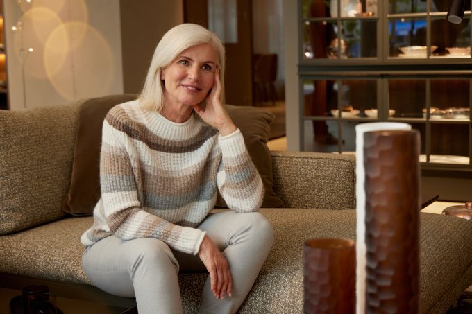 Eine reife Frau sitzt auf der Couch in einem weiß-grauen Streifen Pullover | © Bonita
