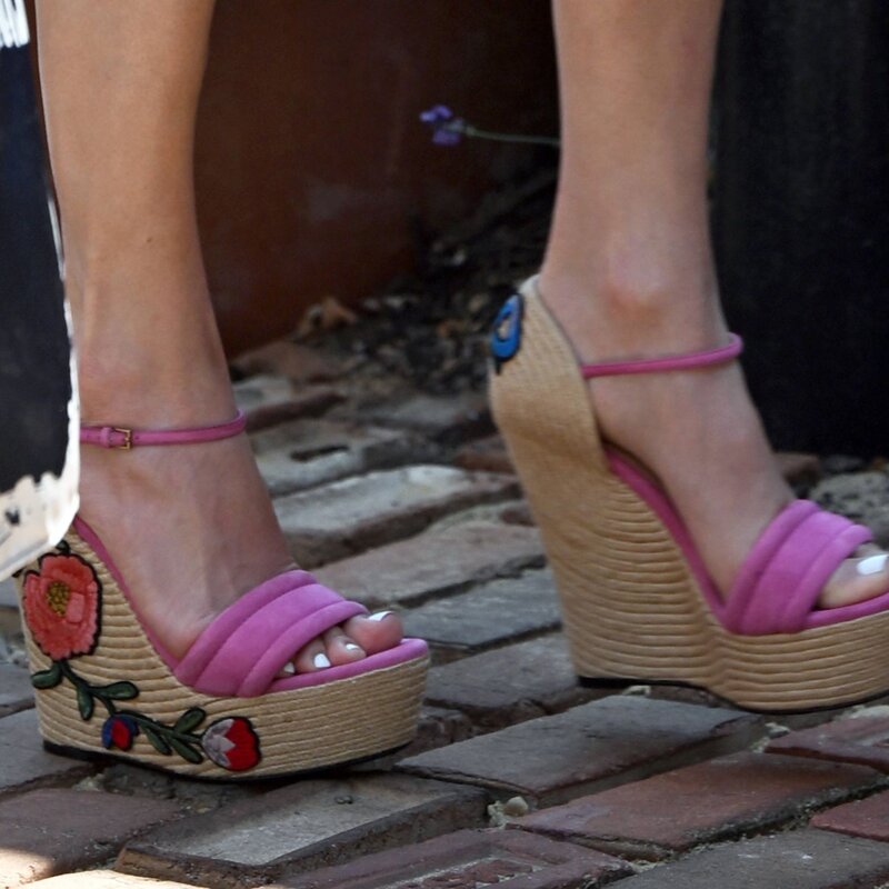 Detailaufnahme pinker Wedges mit Bastsohle und bunter Blumenstickerei auf rotem Pflastersteinboden. | © IMAGO / Cover-Images