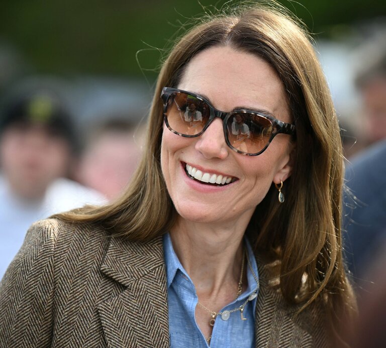 Prinzessin Kate mit glatten braunen Haaren, Sonnenbrille und Ohrhänger trägt braunen Blazer über Jeanshemd in sonniger Menschenmenge. | © IMAGO / i Images