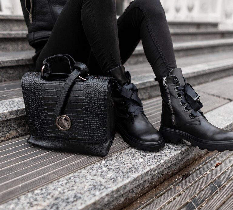 Nahaufnahme von schwarzen Lederstiefeln und einer luxuriösen Handtasche auf einer Treppe aus Stein und Holz. | © Adobe Stock/ alones