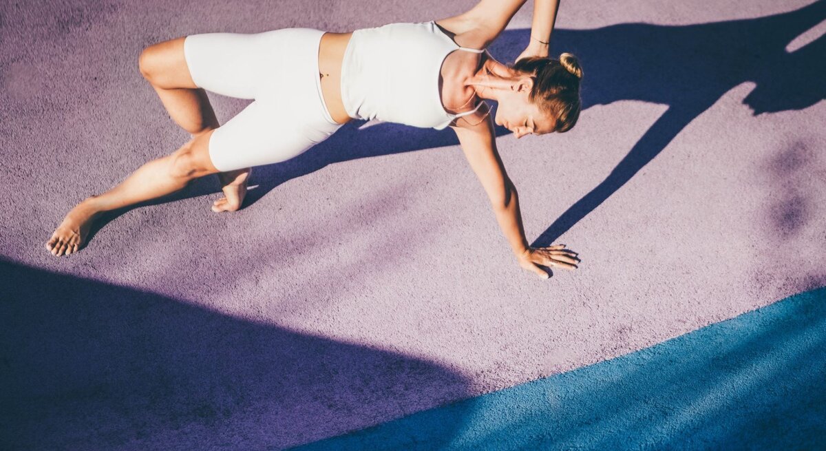 Eine Frau im weißen Sportdress macht Yogaübungen auf dem Boden.