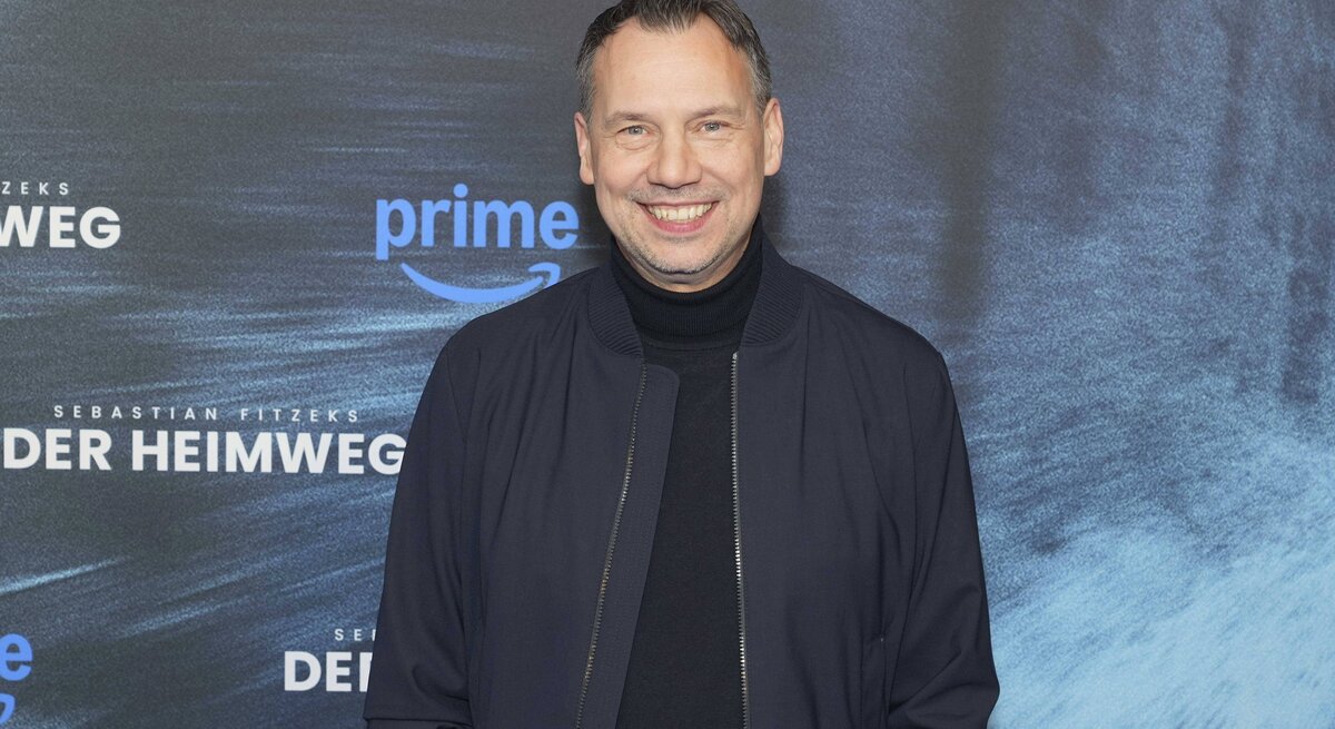 Sebastian Fitzek in dunkelblauer Jacke und schwarzem Rollkragenpullover steht vor einer Fotowand mit Schriftzug und Prime-Logo.