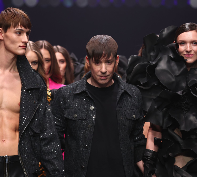 Designer Kilian Kerner mit braunem Pony schreitet mit Models in extravaganten schwarzen und glitzernden Outfits über den Laufsteg. | © Sebastian Reuter