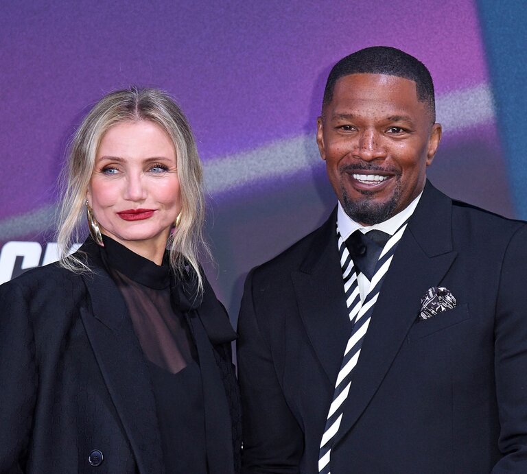 Cameron Diaz mit blonden Haaren, rotem Lippenstift und Jamie Foxx im dunklen Anzug stehen nebeneinander und lächeln vor einer bunten Wand. | © Tristar Media/WireImage