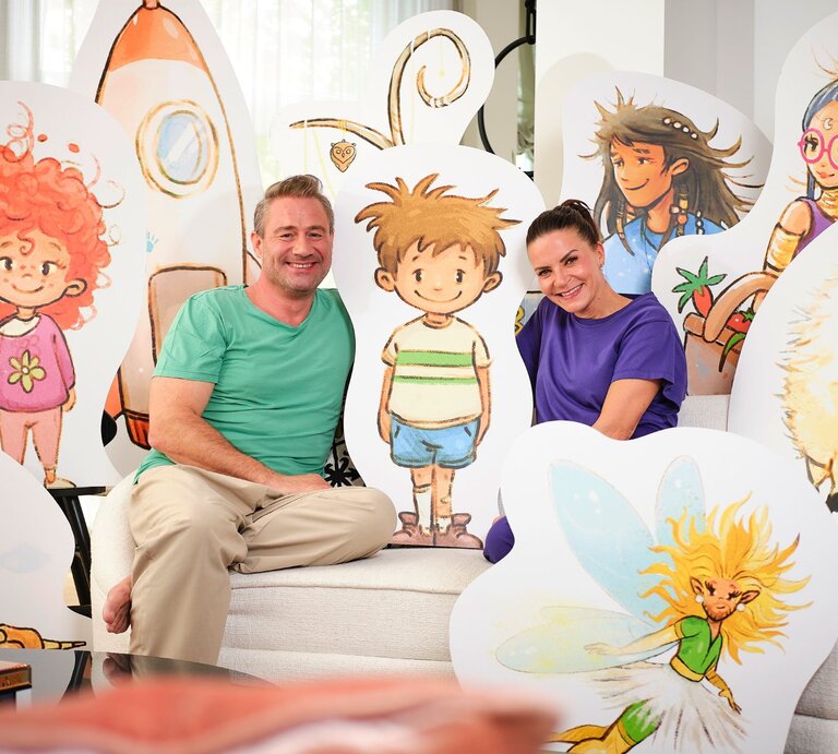 Sänger Sasha mit Ehefrau Julia vor der Kulisse ihres neuen Kinderbuches | © Christian Gehrke