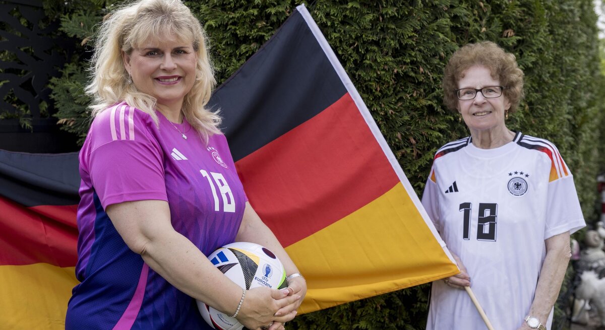 Viola Mittelstädt steht vor einer Deutschlandflagge, die Oma Angelika hält. Beide tragen ein Deutschlandtrikot und Viola hält einen Fußball in der Hand.