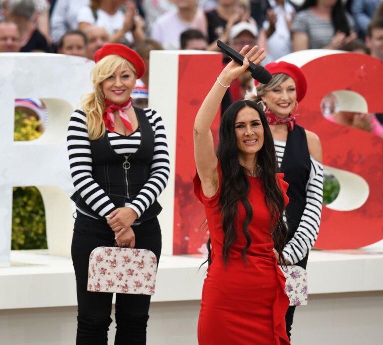 Kiki Cordalis, Tochter von Costa Cordalis, bei einem Auftritt auf einer Bühne. Sie winkt mit einem Mikro in der Hand | © action press