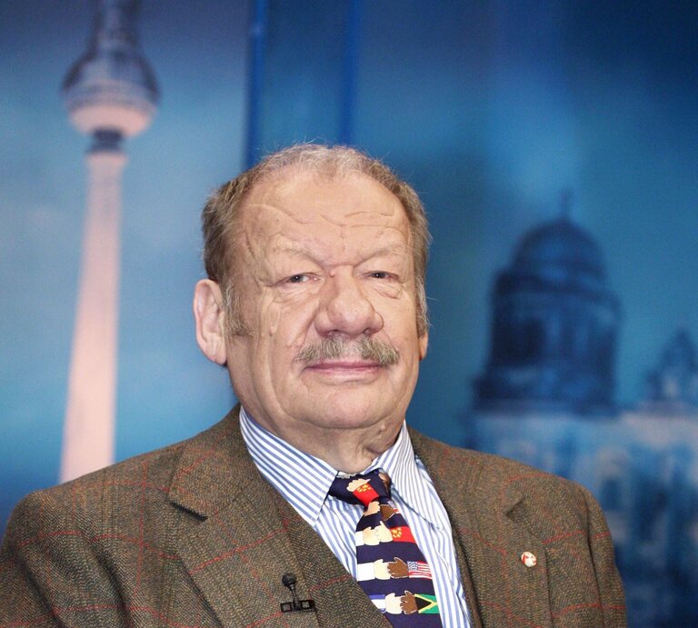 Schauspieler Wolfgang Völz im Anzug schaut ernst in die Kamera, im Hintergrund sind Reichstag und Berliner Fernsehturm als Kulisse zu sehen | © imago / Müller-Stauffenberg