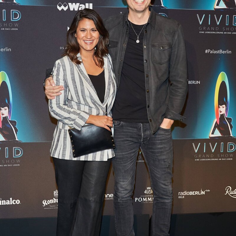Ein Paar in legerer Abendmode, die Frau mit gestreifter Jacke und Clutch, der Mann in schwarzem Outfit und Chelsea-Boots, posiert gemeinsam. | © IMAGO / eventfoto54