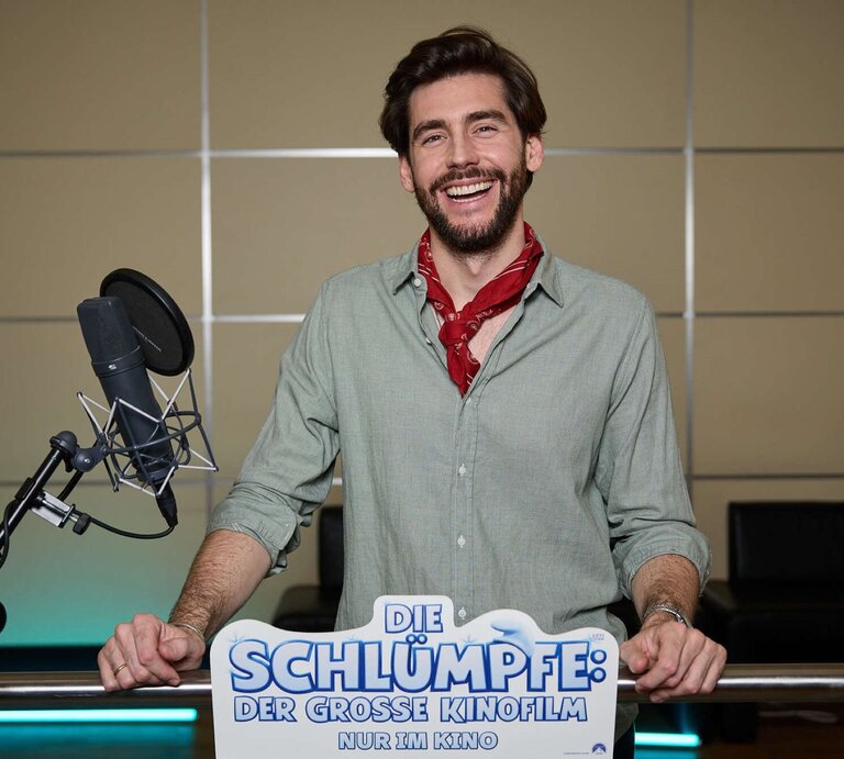 Alvaro Soler mit braunem Bart und grünem Hemd steht vor Mikrofon, während er für "Die Schlümpfe" Werbung macht. | © 2025 Paramount Pictures