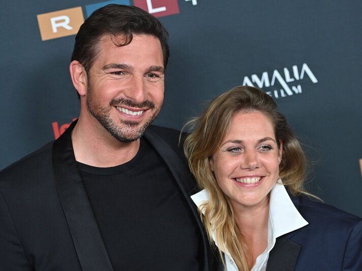 Fröhlicher Mann mit Bart und schwarzem Sakko (Benjamin Max Piwko) steht Arm in Arm mit lachender Frau (Felicitas Woll) im weißen Hemd und Blazer. | © IMAGO / Sven Simon