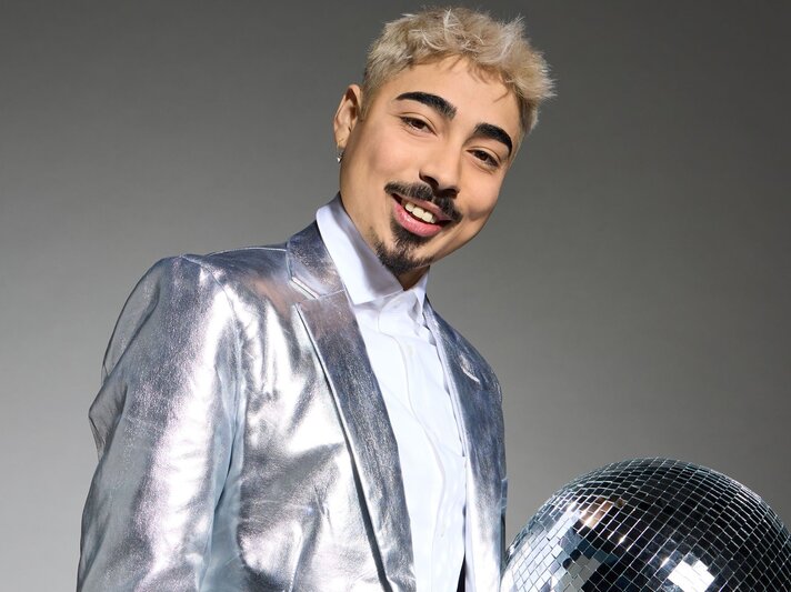 Zu sehen ist ein Portrait von Tony Bauer. Der Mann trägt einen silbernen Anzug, hat blonde Haare, einen dunklen Bart sowie dunkle Augenbrauen und lächelt in die Kamera. | © RTL / Arya Shirazi