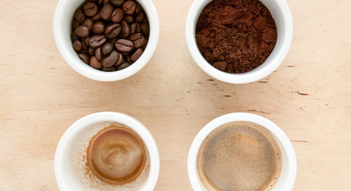 Vier weiße Tassen zeigen Bohnen, Pulver, frischen Kaffee und Kaffeereste als Phasen der Kaffeezubereitung von oben.