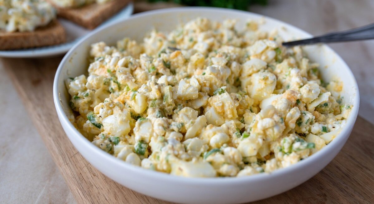 Eiersalat ohne Mayonnaise in runder Porzellanschüssel / Untergrund Holzboden